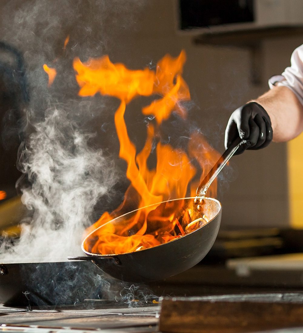 Main d'un cuisinier avec une poêle flambé