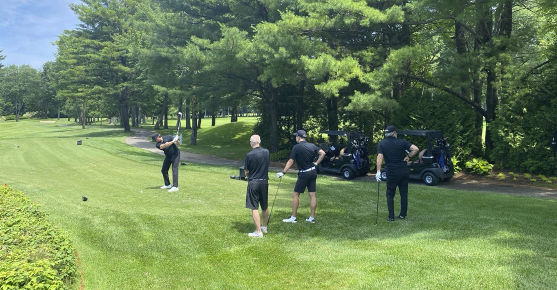 4 hommes habillés en noir au terte de départ d'un trou de golf